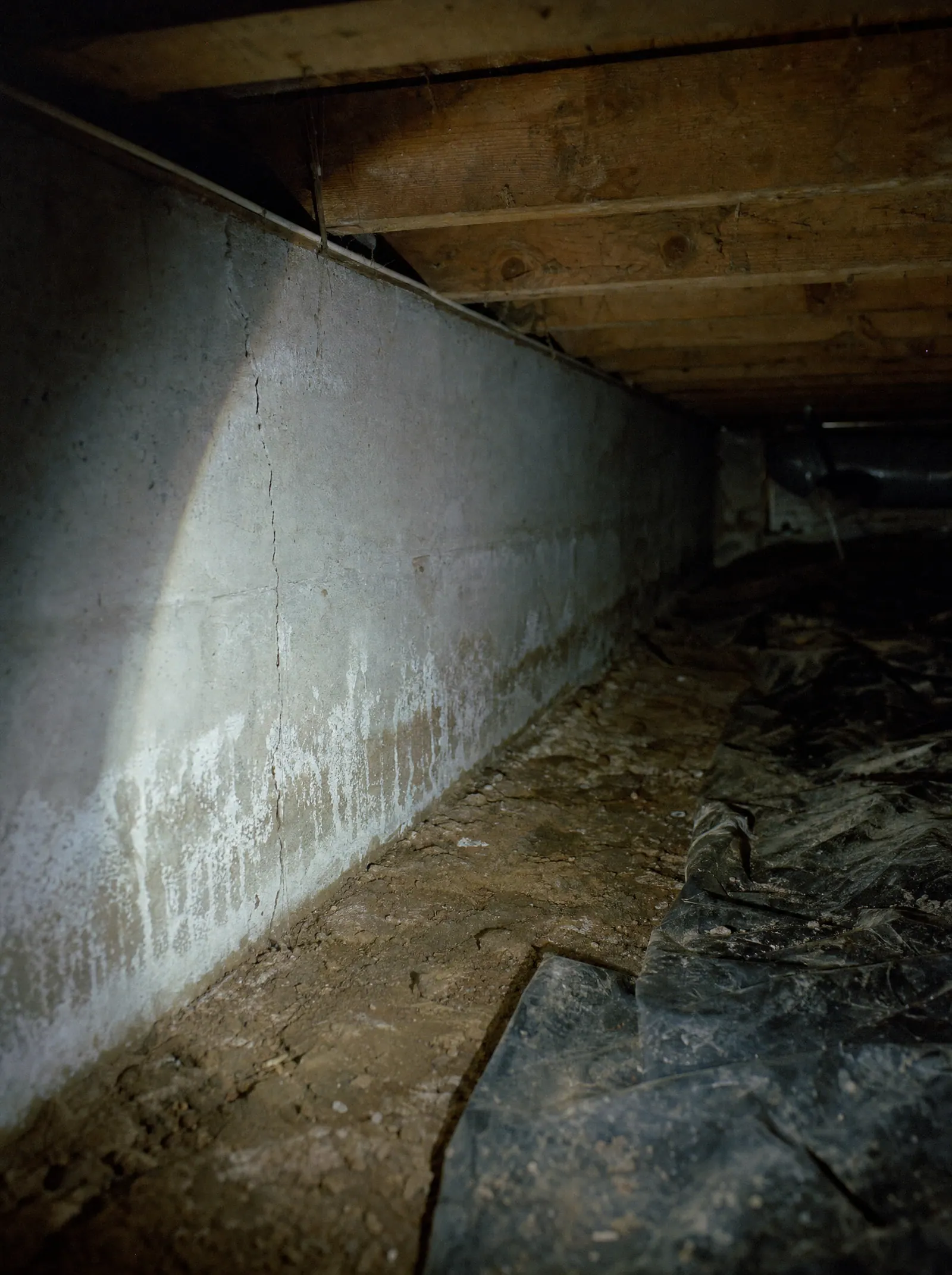 A flashlight raking across a poured concrete foundation wall with a hairline crack and efflorescence